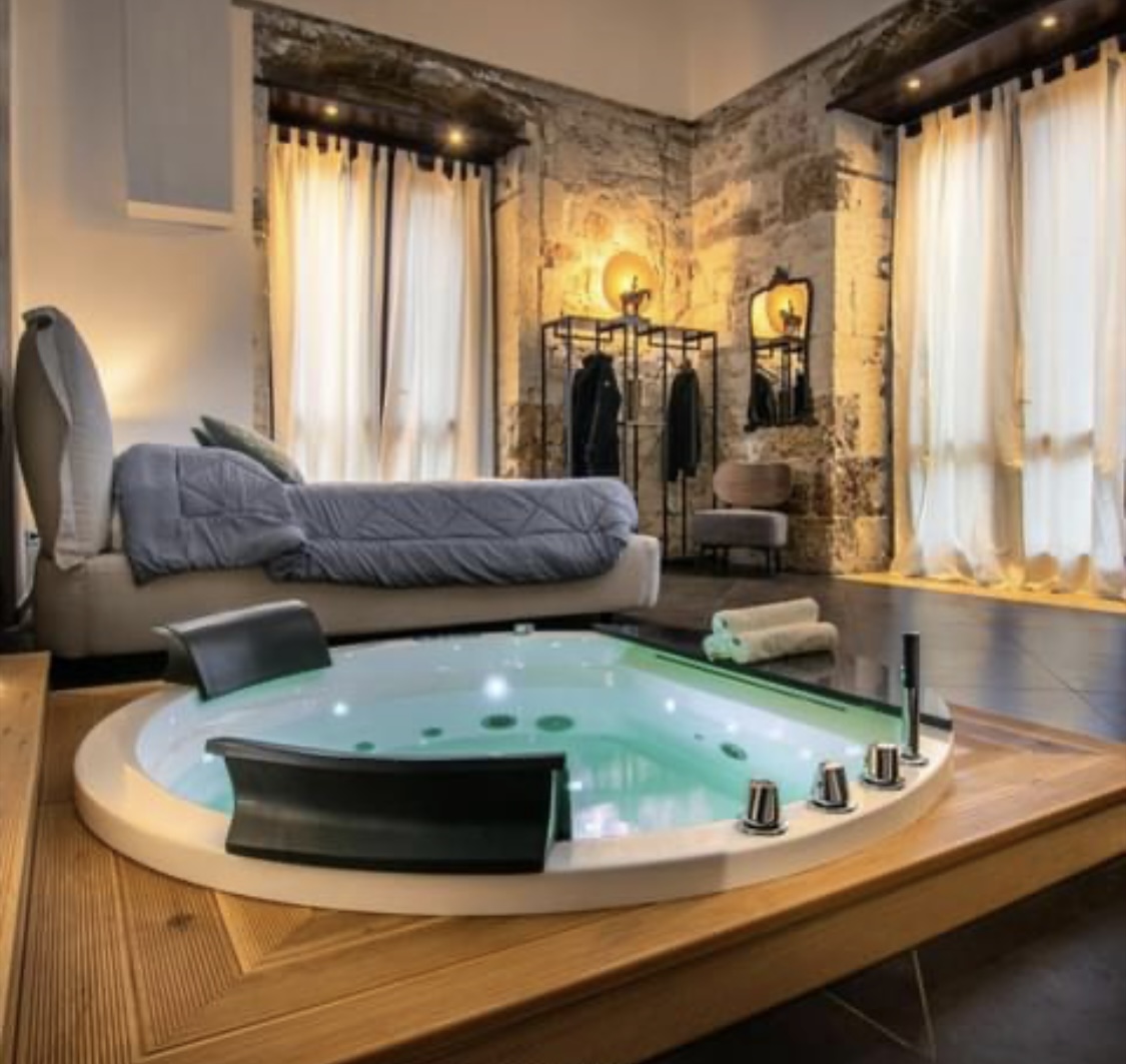 Love room avec jacuzzi central intégré, murs en pierre apparente et lit king-size
